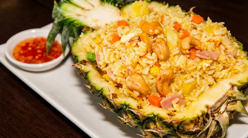 Pineapple fried rice with cashews, ham, and vegetables, served in a pineapple half with chili sauce.