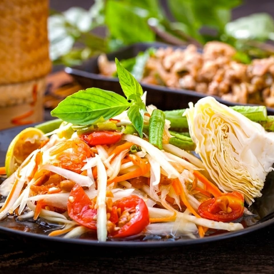 Som Tum (papaya salad) with tomatoes, cabbage, and green beans on a black plate.