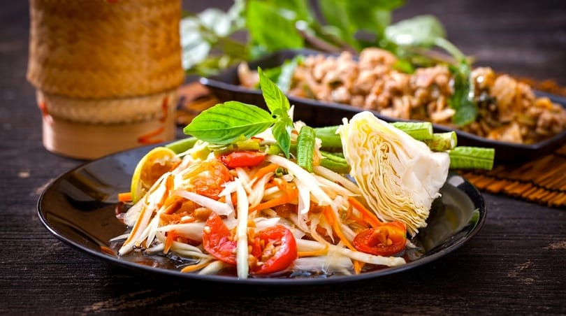 Som Tum (papaya salad) with tomatoes, cabbage, and green beans on a black plate.