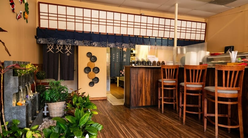Interior of a Japanese restaurant with a sushi bar, wooden stools, and a decorative water feature.